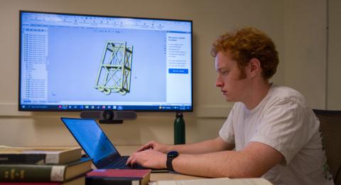 mechanical engineering student looking at a computer with a diagram in the background 