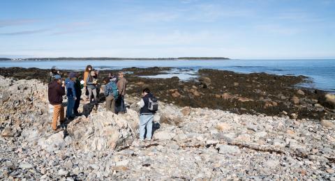 Group of students and professor standing on rocks next to the ocean. 