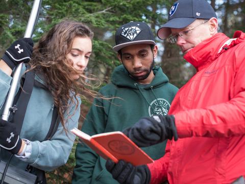 two students and a professor conductiong research outdoors